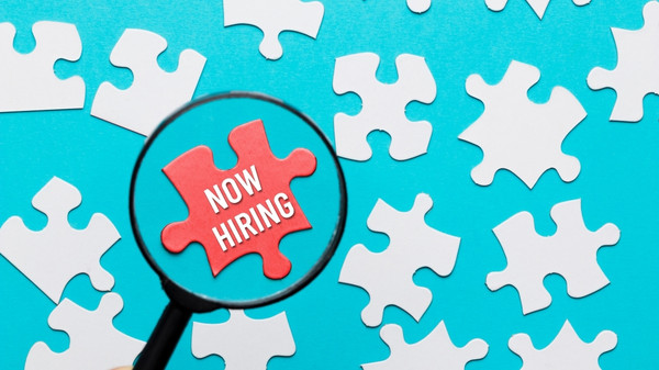 Hiring concept with puzzle pieces and a magnifying glass.